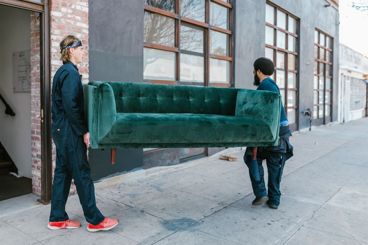 Two-man crew carrying a green couch out of a building during a furniture removal job